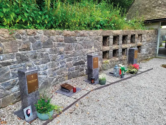 Urnensäulen entlang einer Friedhofsmauer